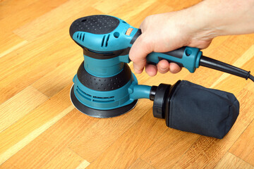 Sanding a wooden floor using an electric sander in a bright room.