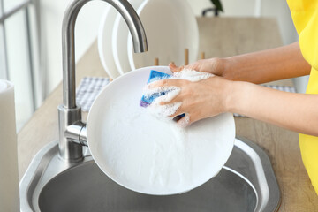 Female janitor with sponge washing plate in kitchen, closeup