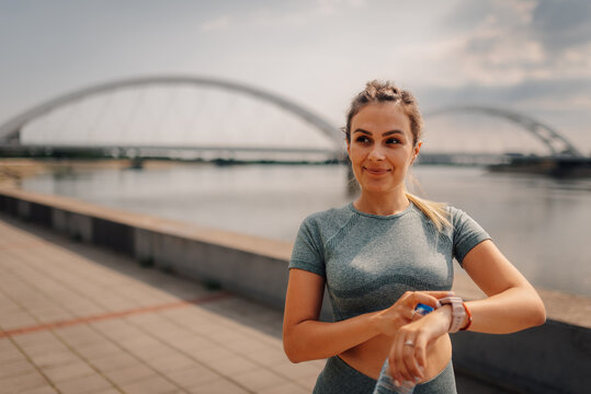 Sportswoman checking smartwatch near river with bridge in background