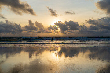 Coucher de soleil sur une plage bretonne avec silhouette dans les vagues et reflets dor&eacute;s sur le sable humide.