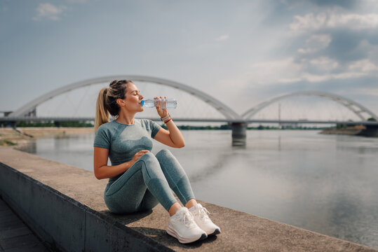 Sporty woman drinking water after training by the river