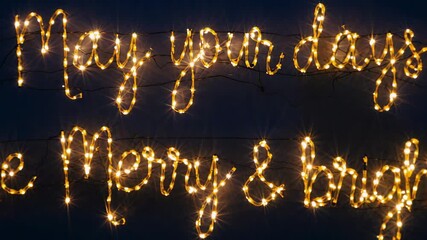 Pulsing scripted string-light sign on dark wall, cable powering bulbs to convey festive message