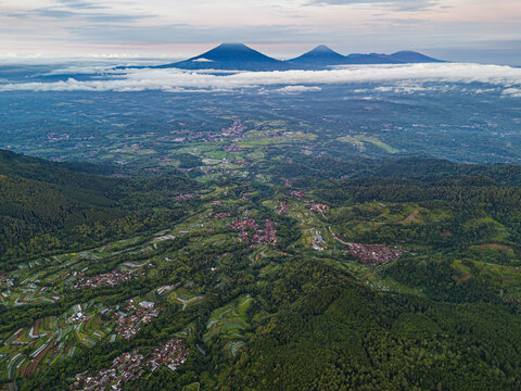 Aerial view of verdant mountains and valleys stretch out beneath a sky kissed with soft clouds, framed by majestic peaks, Magelang, Central Java, Indonesia.