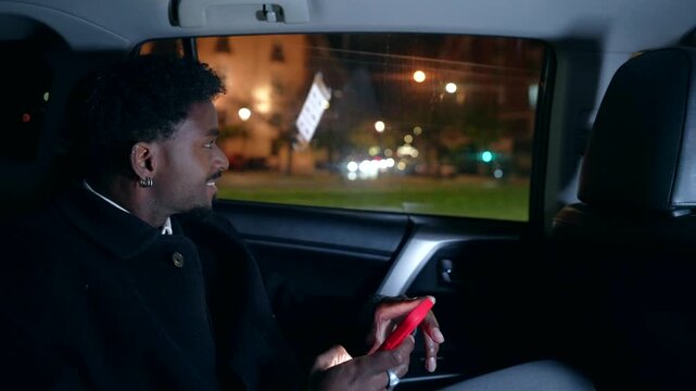 Black man using a smartphone in the back of a moving car at night