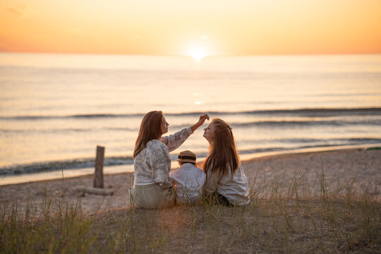 Back view of two caucasian female friends and a child enjoying sunset on the Baltic seashore. 
