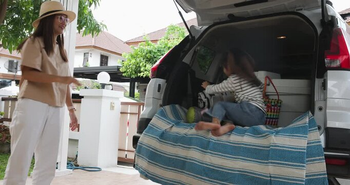 Mother and daughter together loading items into the open trunk of a white car for road trip or family outing travel 