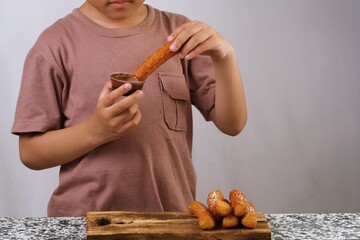 A young boy tasting a churros snack with a curious expression in an indoor studio setting.