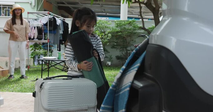 Mother and daughter together loading items into the open trunk of a white car for road trip or family outing travel 
