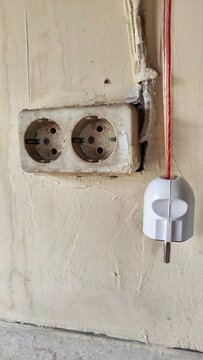 Dilapidated double electrical wall socket with exposed wiring and a detached plug on a dirty building interior surface representing neglected power infrastructure