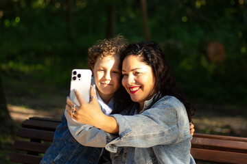 Young mother and son having fun taking selfie with mobile phone in park together. Caucasian mom and boy enjoying making video call with family on smartphone