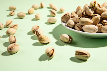 Small plate of pistachios isolated on light green background