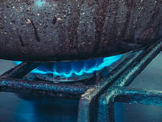 Side view of a brilliant blue gas flame burning under a heavily used, speckled saucepan.