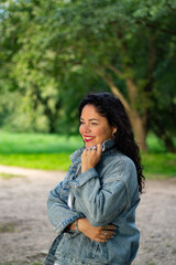 Woman relaxing in green park, smiling. Casual and authentic moment of curly haired woman creating friendly and approachable vibe. Great for relatable content