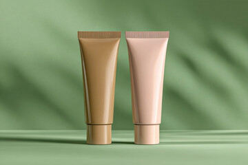 Natural foundation cream tubes.  Brown and pink lotion containers on green background with Light on wall. Mockup