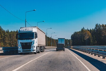 A Scenic View of a Freight Truck Leading a Trailer on an Open Highway Surrounded by Lush Green Forest and Clear Blue Skies