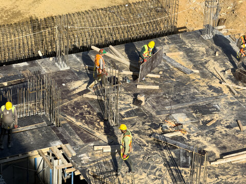 View of construction workers in bright yellow vests and hard hats navigate a busy construction site with rebar and wooden planks, Istanbul, Istanbul, Turkey.