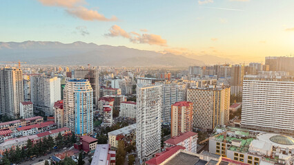 Panoramic view of Batumi, Georgia, showcasing modern high-rise buildings against a backdrop of mountains at golden hour, highlighting the city s blend of urban growth and natural beauty.