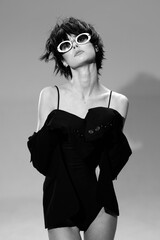 Stylish woman in black dress wearing white sunglasses, posing confidently with short hair in a...