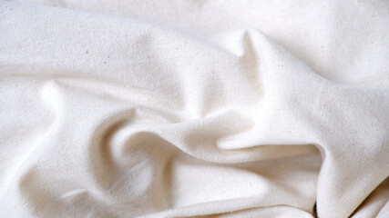 Fototapeta premium Cream calico fabric texture background with abstract folded. Fabric texture background in white-cream. Linen, cloth, minimalist, cozy concept for textile wallpaper, backdrop. Close-up tote bag texture