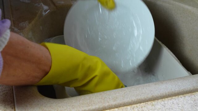 Close view of hands in yellow rubber gloves washing up a white plate, example of household chores