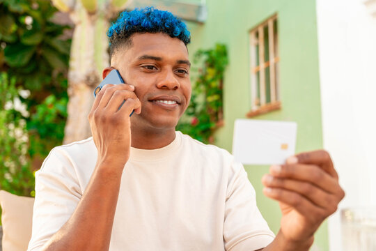 Latin man with blue hair making a mobile payment transaction on smartphone holding credit card