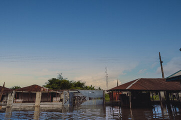 View of floodwaters engulfing homes with rusty roofs under a vast blue sky, reflecting somber tones in Yenagoa, Bayelsa State, Nigeria.