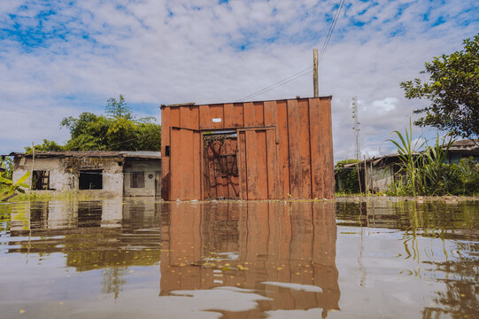 View of a submerged rusty container stands firm amidst the floodwaters reflecting the cloudy sky, with a partially visible building, Yenagoa, Bayelsa Stae, Nigeria.
