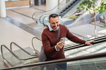 Mature businessman on escalator doing video call on mobile phone