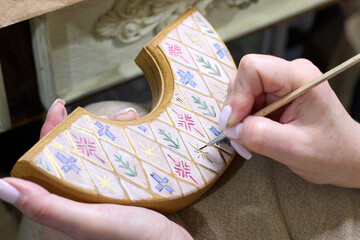 A close-up view showcases a woman's meticulous hand-painting of intricate patterns onto a wooden piece with a fine brush, highlighting the artistry, skill, and dedication involved in handcrafting.