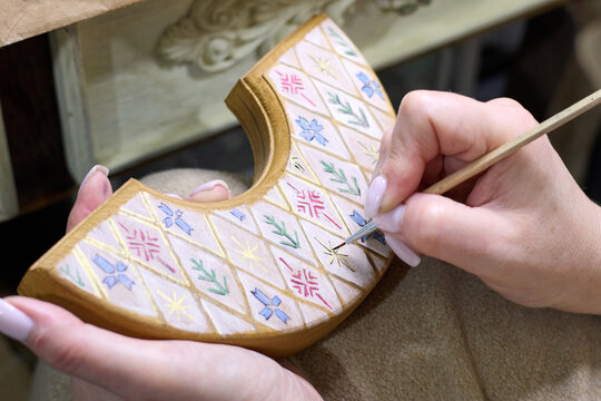 A close-up view showcases a woman's meticulous hand-painting of intricate patterns onto a wooden piece with a fine brush, highlighting the artistry, skill, and dedication involved in handcrafting.