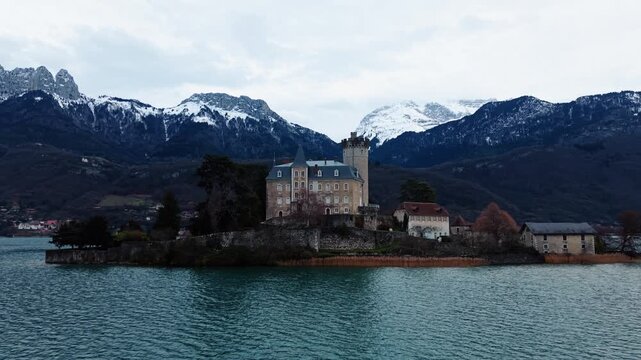 Aerial view of the Chateau de Duingt, a beautiful castle on a small island in a lake, with the snow-capped mountains in the backdrop, Duingt, Auvergne-Rhone-Alpes, France.