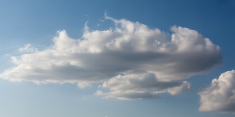 Obraz premium Expansive blue sky with a prominent, elongated white cloud and a smaller fluffy cloud