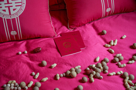 Symbolic 'Zao Sheng Gui Zi' items, including dates, peanuts, longans, and lotus seeds, arranged with Chinese marriage certificates on red wedding bed linen, wishing fertility to newlyweds.