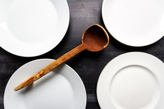 Big white plates and wooden spoon on black chalkboard background. Flat lay. Top view. Food concept. Dark mood food photography.