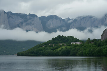 Misty mountain landscape with a serene lake and a verdant hillside village under an overcast sky