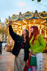 Young friends taking selfie near carousel in city