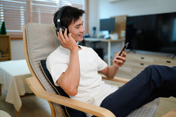Smiling young man wearing headphones listen to mobile music playing in smartphone app, happy guy...