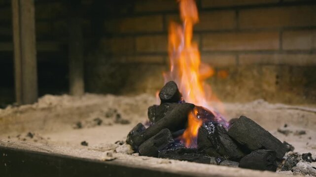 Slow-motion dolly shot of burning charcoal with rising flames, capturing the heat and glowing embers used for a barbecue or fireplace in a warm, rustic setting. High quality FullHD footage