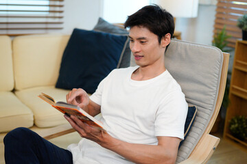 man relaxing at the armchair at home while reading his favorite book