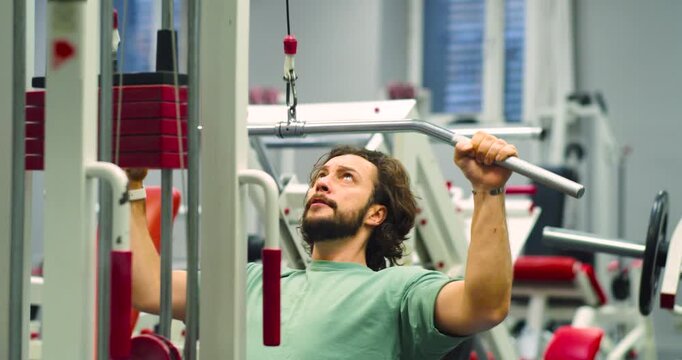 Slow motion close-up 4k footage of a Caucasian man working out in the gym. Workout for back muscles. Physical education as a norm of life for maintaining health.