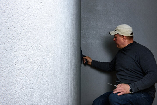 Worker using a float to smooth decorative pebble plaster on a wall.