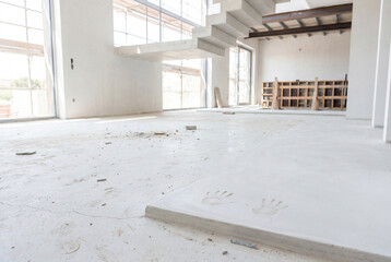 Modern unfinished house interior with concrete staircase, open space and daylight during construction and renovation work