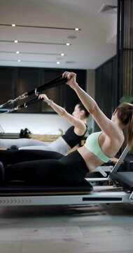 Two individuals perform reformer Pilates exercises in a contemporary gym setting. The atmosphere is lively and focused on fitness, showcasing strength training techniques