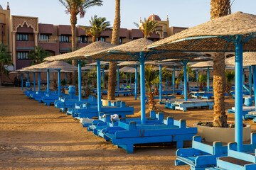 Blue sun loungers and straw umbrellas on a sandy resort beach