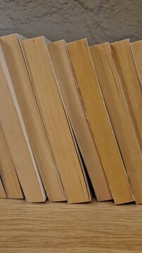 A row of paperback books is neatly exposed on a wooden shelf, showing their aged page edges in warm light. The abstract close-up highlights reading culture, literature and a quiet home library mood.