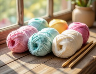 Colorful yarn balls in pastel shades arranged on a wooden surface near a window. Knitting needles are placed beside them, creating a cozy crafting atmosphere.