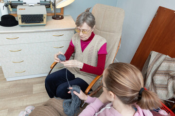 Elderly woman with adult girl preparing yarn for knitting, showing shared hobby and intergenerational bonding during leisure time.