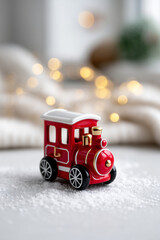 Small red Christmas toy train placed on white snowy surface with golden bokeh lights in the background, minimal composition with copy space on the right, soft pastel holiday colors