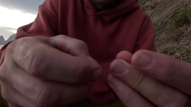 Fishing bait hands, man prepares fishing hook by the sea in the outdoors before an overcast sky