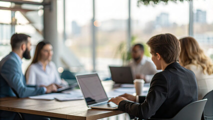 Group of people meeting in a modern office space discussing ideas while working on laptops at midday